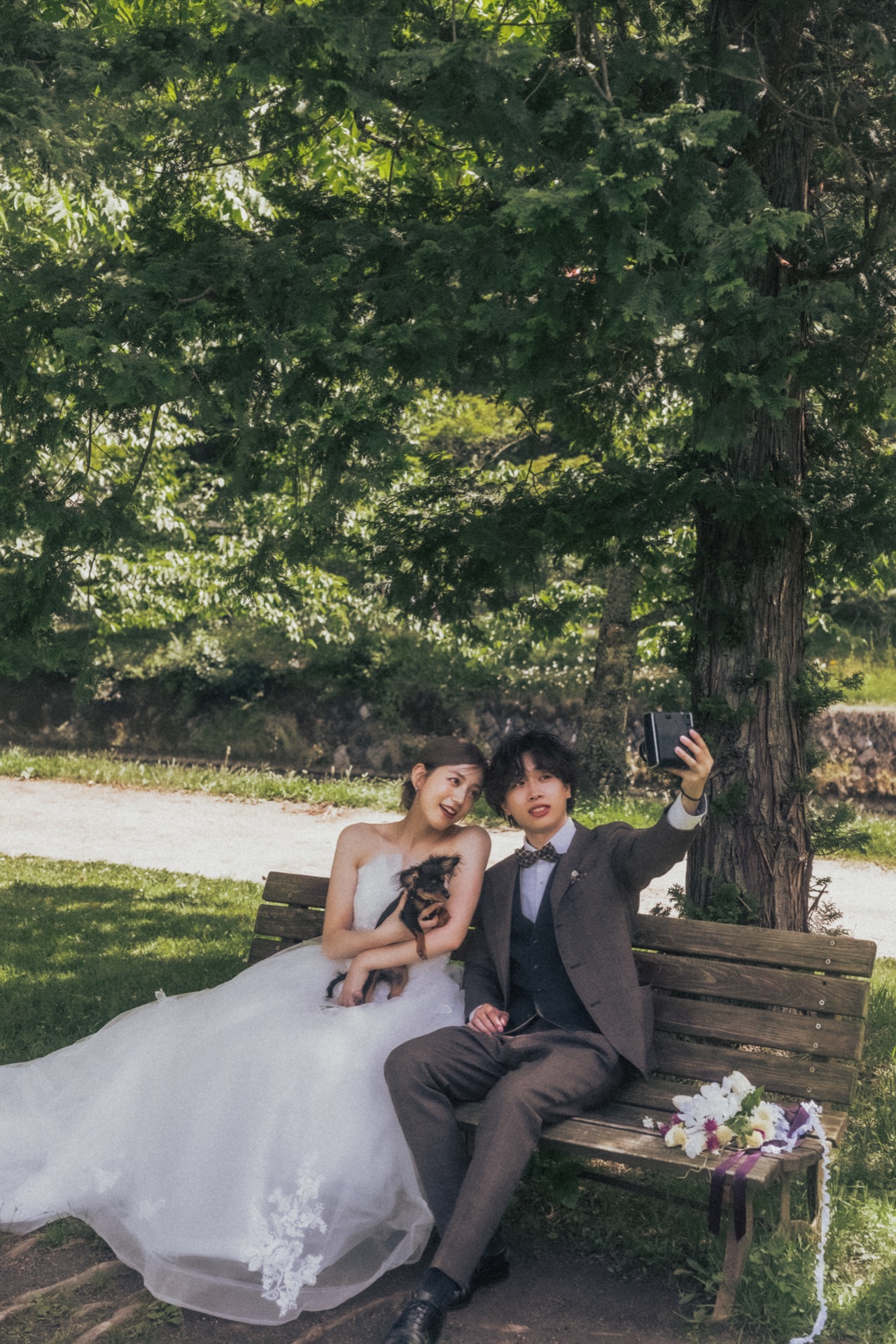 木陰のベンチで愛犬と一緒に過ごす新郎新婦